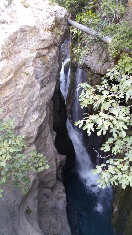 Tall narrow waterfall slot surrounded by rock and vegetation in Kourtaliotiko Gorge